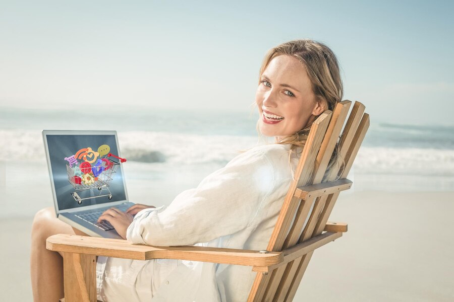 Composite image of gorgeous blonde sitting on deck chair using laptop on beach