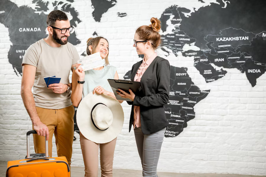 Young couple of travelers choosing a summer strip standing with travel agent on the world map background