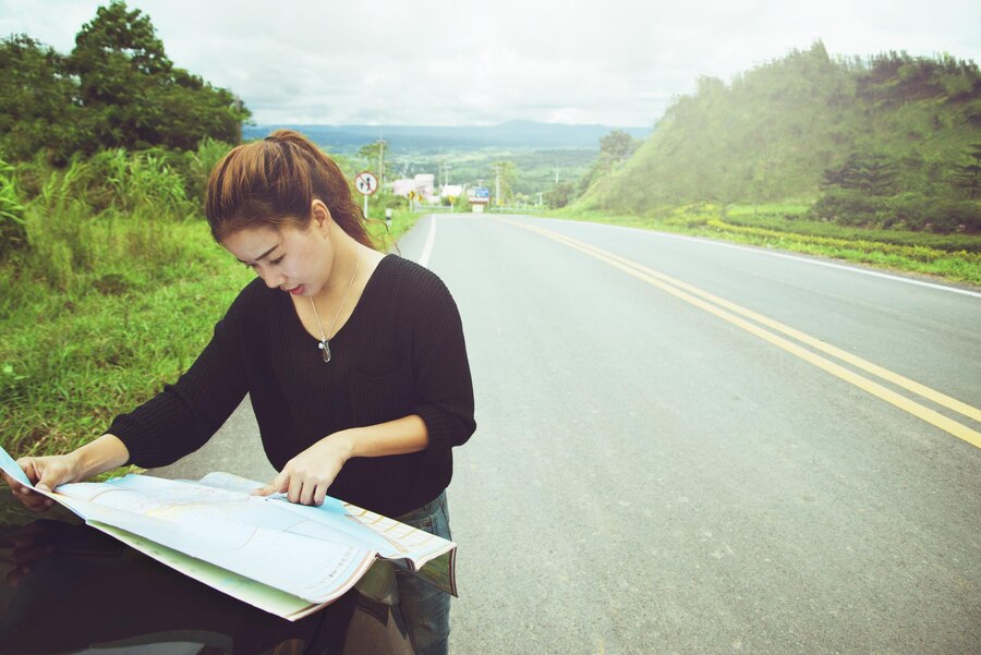 Young woman reading map while standing on road